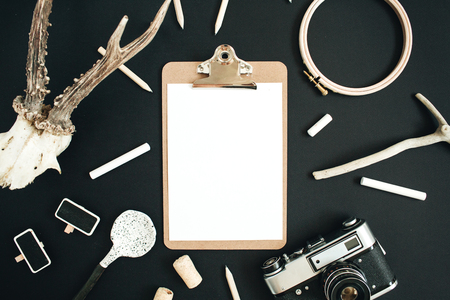 Clipboard mock up with goat horns, retro camera, handmade spoon, pencils and accessories on black chalk board background. Top view, flat lay hipster concept.の写真素材