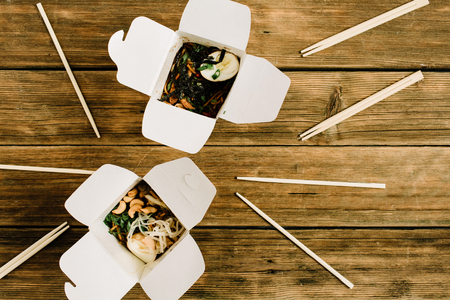 Noodles in box and chopsticks on wooden table background. Flat lay, top view. Chinese takeaway food concept.の写真素材