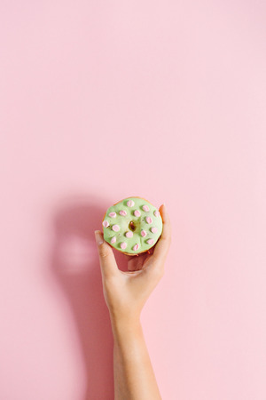 Female hand holding donut on pink background. Minimal flat lay.の写真素材