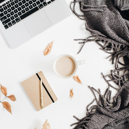 Office desktop with laptop, craft diary, golden pen, terry plaid, fall autumn leaves, coffee with milk on white background. Flat lay, top view.の写真素材