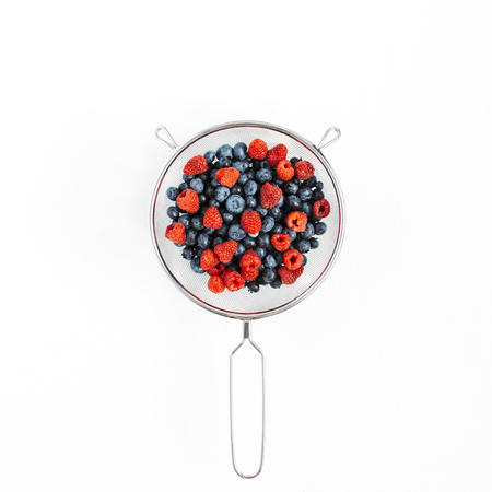 Blueberry and raspberry in colander on white background. Food blog or magazine concept texture.の写真素材