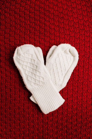 White knitted mittens on red knitted background. Winter minimal background. Flat lay, top view heart symbol. Valentine's Day concept.の写真素材