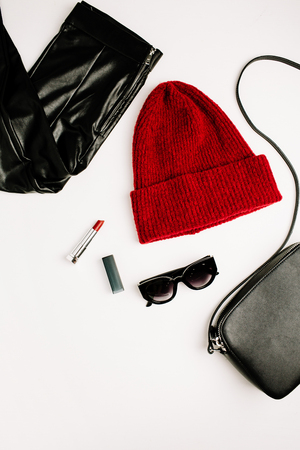Female fashion clothes and accessories on white background. Red hat, black purse, sunglasses, lipstick and leggings. Flat lay, top view look.の写真素材