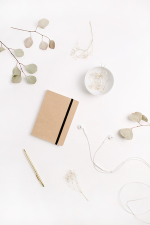 Flat lay home office desk with craft diary, pen, headphones and eucalyptus branches on white background. Top view.の写真素材