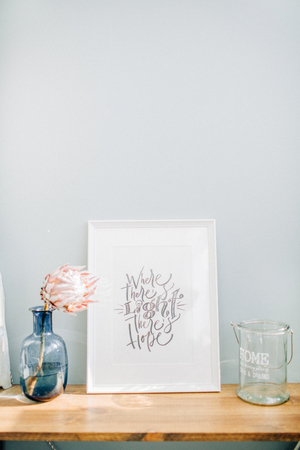 Photo frame with calligraphic quote Where there's light there's hope, protea flower in vase in front...