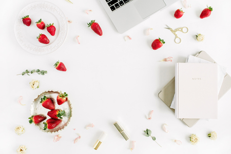 Female modern home office desk with laptop, notebook, lipstick, fresh raw strawberries and rose flower buds on white background. Flat lay, top view. Frame with copy space for text.の写真素材