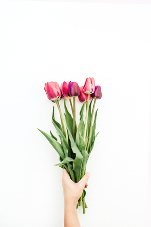 Woman hand holding tulips bouquet on white. Flat lay, top view flowers festive background.の写真素材