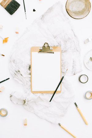 Flat lay, top view artist home office workspace desk with clipboard mockup, paint brushes, blanket and tools on white background.の写真素材