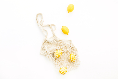 Fresh raw lemons in string bag on white background. Flat lay, top view summer concept.の写真素材