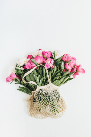 Pink and white peony flowers in string bag isolated on white background. Flat lay, top view minimal floral concept.の写真素材