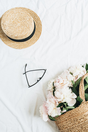 Creative female concept with white peony flowers bouquet in straw bag, glasses and straw hat on white background. Flat lay, top view fashion or beauty blog template.の写真素材