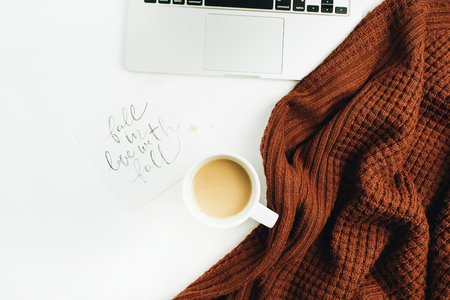 Hand lettered quote "Fall in love with fall", laptop, coffee, warm pullover on white background. Flat lay, top view autumn office desk workspace.の写真素材