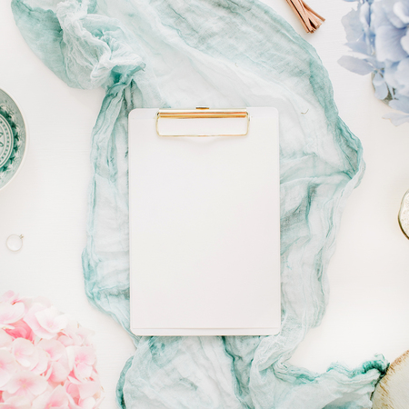 Home office desk with clipboard with copy space, turquoise blanket, colorful pastel hydrangea flower bouquet, woman fashion accessories on white background. Flat lay, top view workspace mockup.の写真素材