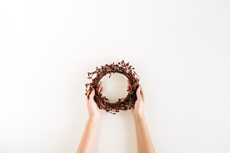 Wreath frame of red berries in female hands on white background. Flat lay, top view Christmas / New Year mockup composition.の写真素材