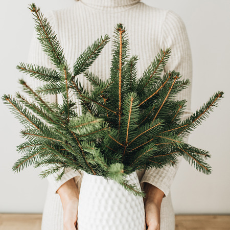 Young pretty woman in white dress holding vase with fir branches bouquet.の写真素材