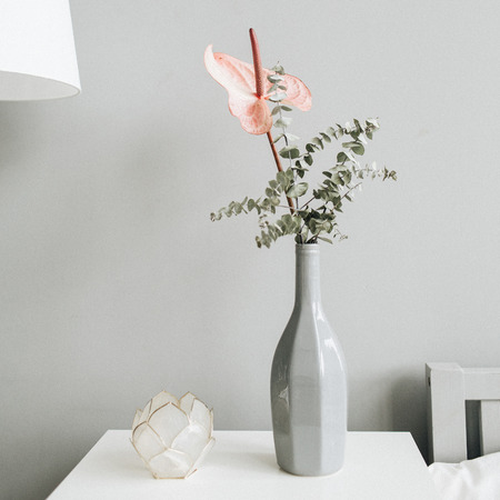 Floral bouquet of pink anthurium flower and eucalyptus branch in bottle on table at pastel wall. Minimal modern trendy interior design concept.の写真素材