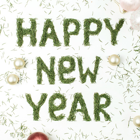 Quote HAPPY NEW YEAR made of spruce needles and Christmas balls decorations on white background. Flat lay, top view New Year composition.の写真素材