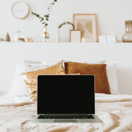 Relax, chill with laptop in bed with pillows. Apartment interior design concept. Freelancer, blogger composition. Blank mockup screen hero header for blog, website, social media.の写真素材
