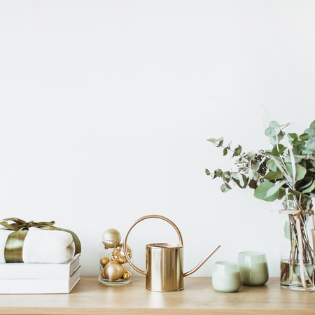 Modern interior design concept. Minimal Nordic Scandinavian style living room with wooden table with gift box, floral bouquet with eucalyptus, candles, radio at white wall. Pastel apartment for rent.の写真素材