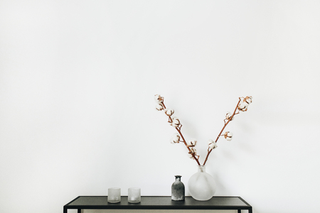 Modern scandinavian interior design concept. Stylish rack with cotton branch in vase, candles at white background.の写真素材