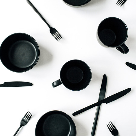Black trendy kitchenware: forks, knifes, mugs, bowls on white background. Flat lay, top view modern kitchen minimal concept.の写真素材