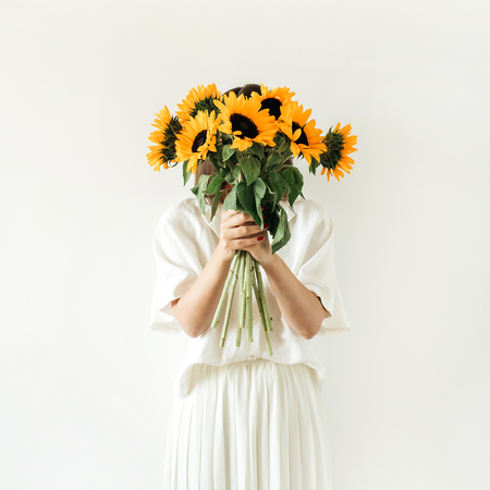 Young pretty woman in white dress hold sunflowers bouquet on white background. Florist minimal concept.の写真素材