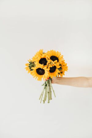 Women's hand hold yellow sunflowers bouquet on white background. Flat lay, top view summer floral concept.の写真素材
