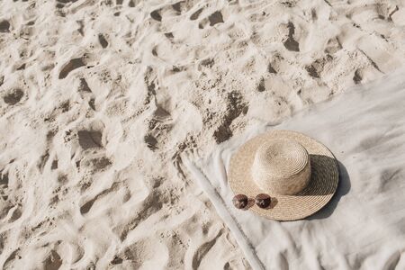 Tropical beautiful beach with white sand, foot steps, neutral blanket with straw hat and sunglasses. Summer travel or vacation concept. Minimalistic background. Top view, flat layの写真素材