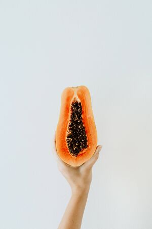 Summer and travel concept. Young woman's hand holding exotic tropical orange papaya fruit. Minimalistic seasonal vegetarian or vegan background.の写真素材