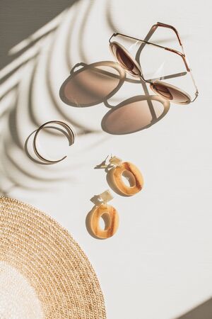 Fashion composition with women's accessories on white background with floral shadow. Earrings, sunglasses, bracelet, straw hat on white background. Flat lay, top view trendy french style lifestyle blog concept.の写真素材