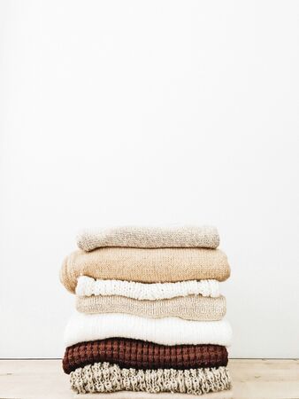 A minimal stack of warm beautiful feminine sweaters or pullovers lying on wooden table agains white wall. Autumn, fall, winter, fashion concept. Empty space, mock up.の写真素材