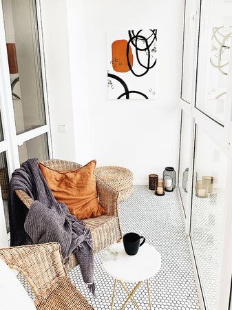 Modern Nordic Scandinavian interior design. Bright open space at loggia with white walls, straw chairs, marble table, ginger pillow, candles, modern painting. Elegant apartment for rent concept.の写真素材