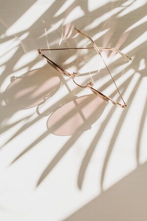 Pink women's sunglasses on white table with floral shadow. Fashion trendy french style lifestyle...