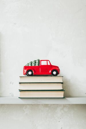 Christmas / New Year composition. Traditional toy of christmas red car with fir on the roof standing on books. Minimal winter holidays concept. Christmas card.の写真素材