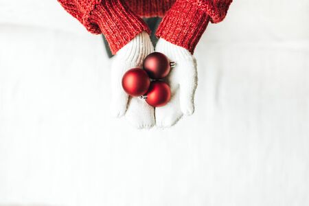 Christmas / New year / xmas composition. Young woman in red knitted sweater and white mittens holding tree red christmas toys. Flat lay, top view. Minimal winter holidays concept.の写真素材