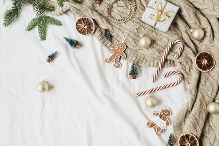 Christmas / New Year composition. Gift box, fir branches, Christmas baubles, ginger cookies, stick candies, knitted plaid, decorations. Flat lay, top view decorated holiday background.の写真素材