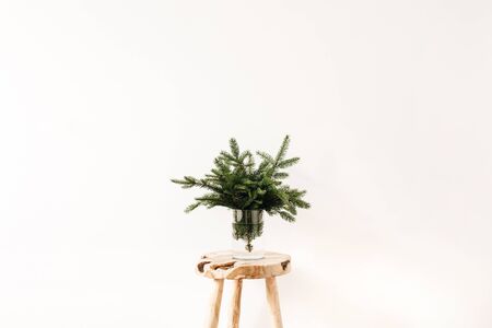 Bouquet of fir-tree branches on solid wooden stool on white background. Minimal Christmas, New Year composition.の写真素材