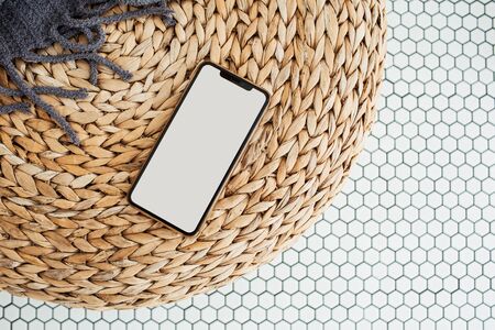 Blank screen cell phone with empty copy space mockup on rattan puff, plaid and mosaic tile. Flat lay, top view template for social media, website, blog, magazine.の写真素材