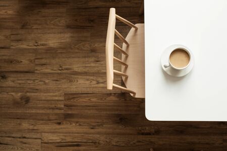 Cup of coffee with milk on white table near designer chair and wooden floor. Top view modern...