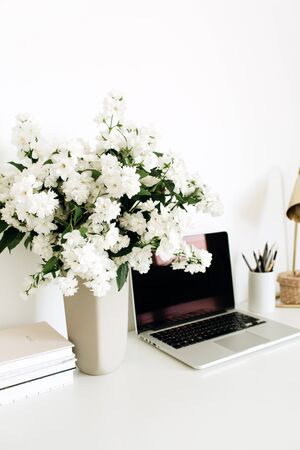 Laptop with mockup blank copy space screen on table. Office desk workspace with flowers bouquet, table lamp. Minimal freelance co-working concept.の写真素材