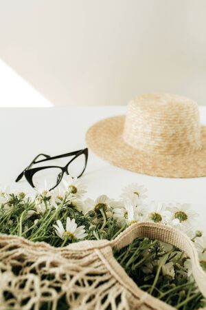 Minimal fashion concept with straw hat, chamomile daisy flowers bouquet in string bag, glasses.の写真素材
