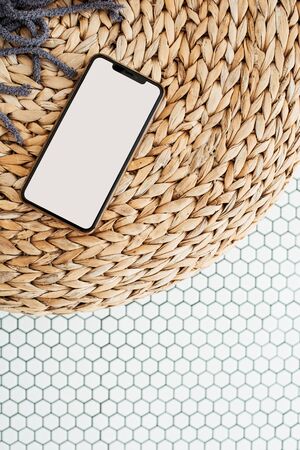 Blank screen smartphone with empty copy space mockup on rattan puff and mosaic tile. Flat lay, top view template.の写真素材