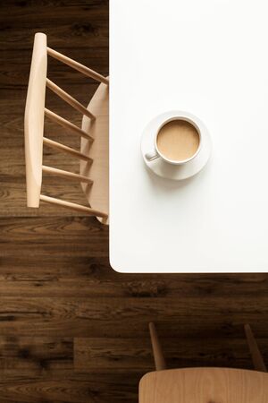 Cup of coffee with milk on white table near designer chair and wooden floor. Top view modern interior design furniture concept.の写真素材