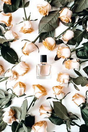 Flat lay women's perfume bottle in frame of rose flowers on white background. Top view perfumery,...