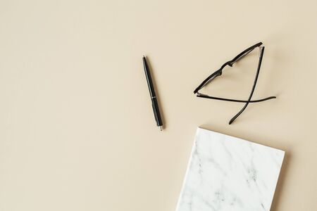 Marble styled notebook, pen, glasses on pastel beige background. Minimalist home office desk table. Flat lay, top view woman lifestyle business concept.の写真素材