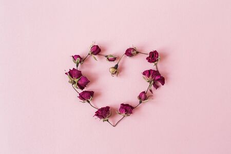 Heart symbol made of dry rose flower buds on pink background. Flatlay, top view Valentine's Day minimal holiday concept.の写真素材