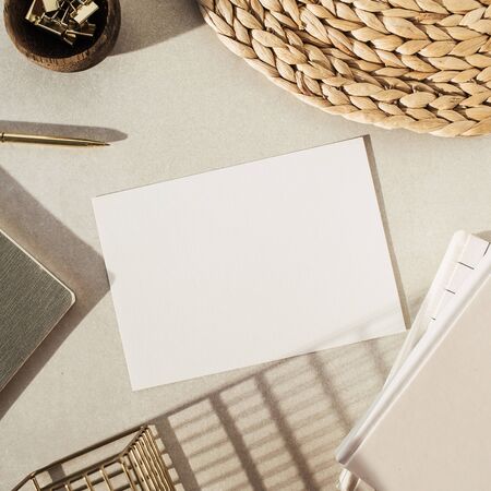 Flatlay blank paper sheet, notebooks, clips in wooden bowl, straw stand on beige concrete...