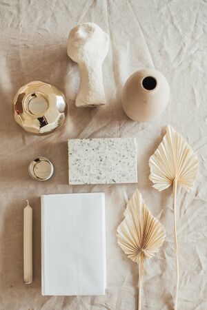 Lifestyle, still life composition with home decoration: book, fan leaves, granite brick, bust, candle, on beige linen table cloth. Flat lay, top view.の写真素材