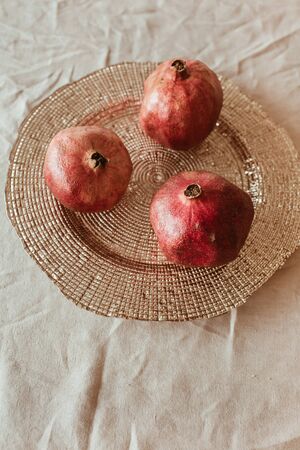 Three pomegranates on golden plate on beige table cloth.の写真素材