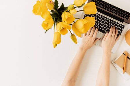 Women's hands typing on laptop. Home office desk workspace with laptop, tulip flowers bouquet on white background. Flat lay, top view, overhead viewの写真素材